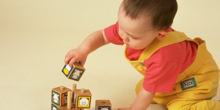 ca. 1991 --- Young Eleanor plays with a puzzle putting cubes onto one of four pegs at the age of 19 months. --- Image by © Laura Dwight/CORBIS